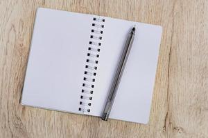 affärs- och kontorskoncept - tom anteckningsbok en svart penna på träbord. minimal platt läggning, ovanifrån. foto