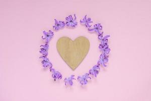 rund ram av pastell lila hyecinth blommor och trä hjärta på gradient rosa bakgrund. blomkrans. layout för semester hälsning av mors dag, födelsedag, bröllop eller annan glad händelse foto