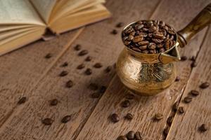 färska rostade kaffebönor i cezve traditionell turkisk kaffekanna öppnad bok och kopp på träbord. foto