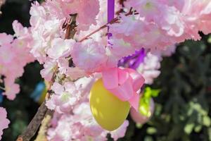 gult påskägg hänger på blommande äppelträdsgren. påsk dekoration och firande koncept. foto