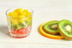 kost färsk välsmakande mix fruktsallad i en glasburk på träbord. hackade saftiga apelsiner, kiwi och grapefrukt. foto