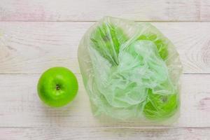 färska gröna äpplen i plastpåse på träbord. miljökonceptet för icke-ekologisk användning av plast foto