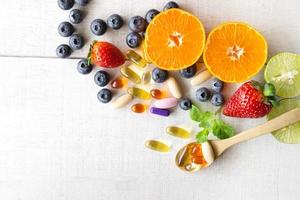 multivitaminer och kosttillskott med färska och hälsosamma frukter på vit trä bakgrund. foto