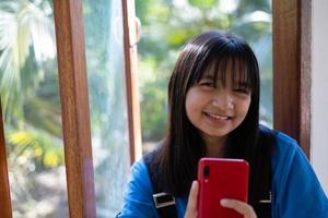 Lycklig ung flicka använder sig av mobil telefon och Sammanträde på de fönster på Hem. foto