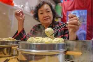 defokusering senior asiatisk kvinnor äter små ånga bullar i kinesisk restaurang.beijing huvudstad stad av Kina foto