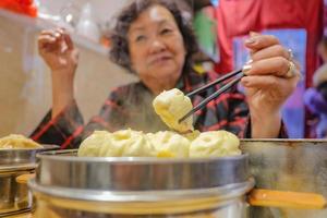 defokusering senior asiatisk kvinnor äter små ånga bullar i kinesisk restaurang.beijing huvudstad stad av Kina foto