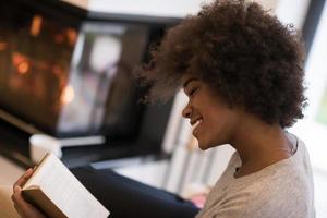 svart kvinna läser bok framför öppen spis foto