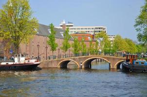 skön flod med fartyg, hermitage och amstel bro i amsterdam, holland nederländerna foto