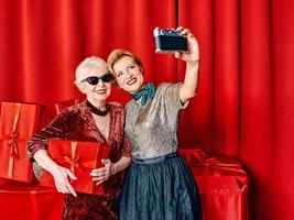 två senior kvinnor på de fest framställning selfie innehav mobiltelefon på selfie pinne. fest, firande, teknologi begrepp foto