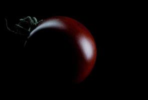 svart tomat på en svart bakgrund. körsbär tomat är cumato på en svart bakgrund. foto