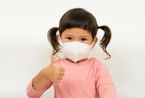 liten asiatisk flicka bär mask för skydda PM 2,5 och visa tummen upp gest för Bra luft utomhus.luft förorening PM 2,5 och coronavirus begrepp foto