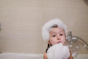 liten flicka i bad spelar med tvål skum foto