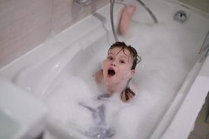liten flicka i bad spelar med tvål skum foto