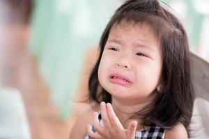 ett asiatisk liten barn flicka är gråt, ledsen tårar från varelse skällde ut förbi ett vuxen. bebis unge 3 år gammal. i de sommar tempel område. de begrepp av sorg för ung barn. foto