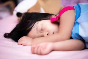 asiatisk barn är sovande på en rosa säng. unge omslag de trasa med en blå filt. barn sömn sött. förtjusande barn resten och sömn i de eftermiddag. bebis åldrig 3 år och 5 månad. foto