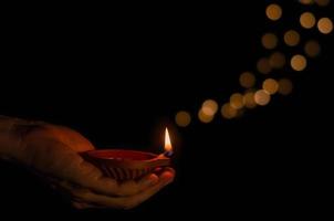 hand innehav de lera diya lampa belyst på mörk bakgrund med bokeh lampor. diwali festival begrepp. foto