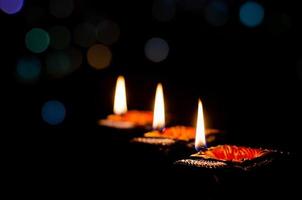 selektiv fokus på flamma av lera diya lampor belyst på mörk bakgrund med färgrik bokeh lampor. diwali festival begrepp. foto