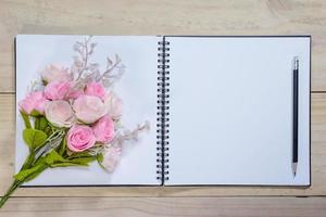öppen notera bok med rosa reste sig blommor på trä- bakgrund foto