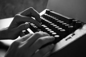 stänga upp av manlig händer skriver på de gammal skrivmaskin. svart och vit tona foto