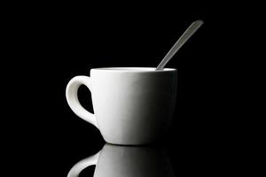 vit kopp med sked på svart bakgrund. foto