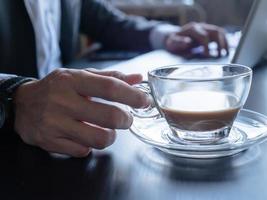 stänga upp av affärsman dricka kaffe och använder sig av en bärbar dator på de kontor skrivbord. foto