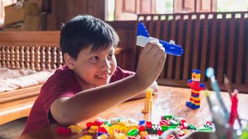 asiatisk pojke är få kreativ med montering färgrik plast tegelstenar in i robotar och plan på en trä- tabell Lycklig och roligt på home.kid skapare begrepp. foto
