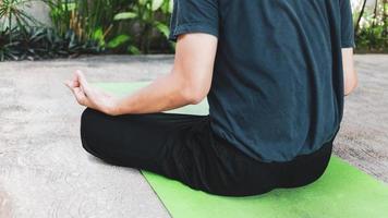 ung asiatisk man praktiserande yoga, andas, meditation, Adha träning, padmasana, halv lotus utgör med lera utgör på de grön yoga matta. övning i de trädgård.frisk levande begrepp foto