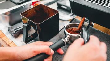 närbild Barista häller nyligen jord kaffe bönor i en portafilter förbi de kaffe kvarn till göra kaffe för kunder i de Kafé foto