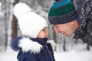 pappa och dotter se på varje Övrig nära i värma kläder, hattar med en pompom på de gata i vinter. familj utflykt, aktiva underhållning, föräldraskap. foto