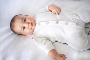 söt porträtt av en bebis i en spjälsäng närbild. en barn i vit kläder på vit underkläder. ömhet och vård, barns problem. foto