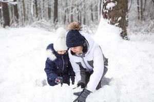 mamma och dotter spela snö spel, bygga en fästning, göra snöbollar. vinter- underhållning utanför, aktiva rekreation, roligt i de kall i värma kläder. utomhus- rekreation, roligt barndom, stark familj foto