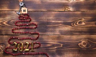 nyckel till huset med en nyckelring på toppen av julgranen gjord av röda fyrkantiga pärlor. platt låg på trä bakgrund. bygga eller köpa hus på nyår. inteckning, fastighetsuthyrning. utrymme för text foto