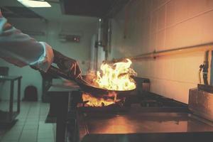 kock håller på med flambe på mat foto