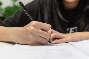 asiatisk studentflicka skriver läxor och läser bok vid skrivbordet foto