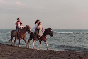 de familj spenderar tid med deras barn medan ridning hästar tillsammans på en skön sandig strand på solnedgång. foto