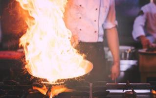 kock håller på med flambe på mat foto