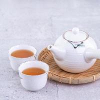 varm te i vit tekanna och koppar på en sikt över ljus grå cement bakgrund, närbild, kopia Plats design begrepp. foto