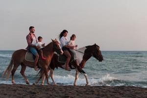 de familj spenderar tid med deras barn medan ridning hästar tillsammans på en sandig strand. selektiv fokus foto