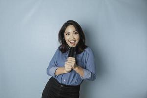 porträtt av sorglös asiatisk kvinna, har roligt karaoke, sång i mikrofon medan stående över blå bakgrund foto