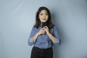 porträtt av en omtänksam ung tillfällig flicka bär en blå skjorta ser åt sidan medan innehav smartphone isolerat över blå bakgrund foto