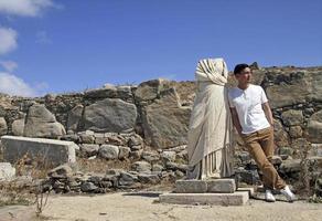 stilig man lutande mot antik staty i mykonos, grekland foto