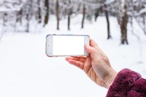hand innehar smartphone med Skära ut skärm i vinter- foto