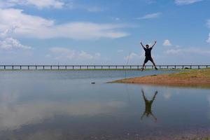 asiatisk man Hoppar över sjö medan resa till lopburi thailand i sommar semester foto