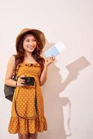 uttrycksfull turist kvinna i sommar tillfällig kläder, hatt innehav pass, biljetter isolerat på beige bakgrund. kvinna reser utomlands till resa helger flykt. luft flyg resa begrepp foto