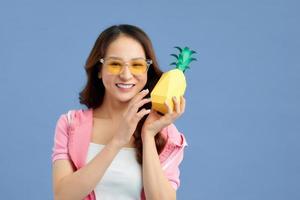 mode sommar porträtt asiatisk flicka i solglasögon och papper ananas över blå bakgrund foto