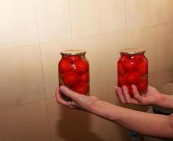 de bearbeta av bevara tomater för de vinter. kvinna händer håll burkar med mogen röd saftig inlagd tomater. foto