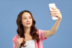 ung attraktiv asiatisk flicka har videosamtal telefon i hand, skytte selfie på främre kamera isolerat på blå bakgrund. foto