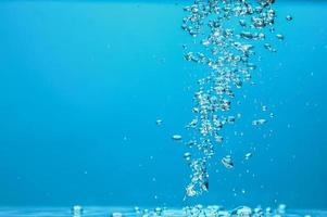 abstrakt bakgrundsbild av bubblor i vatten. rent vatten med vattendroppar och vågor. färskvatten ett glas med bubblor blå bakgrund. foto
