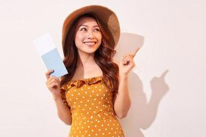 en ung kvinna i en orange polka prickar klänning med en sugrör hatt på henne huvud är innehav en pass och plan biljetter foto