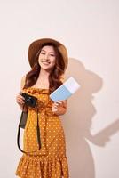 porträtt av en Lycklig ung kvinna i hatt innehav kamera och som visar pass medan stående isolerat över beige bakgrund foto